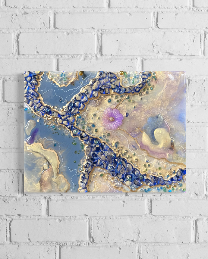 Epoxy resin geode abstract of pearl and blue colors with a purple flower in center hanging on a white brick wall