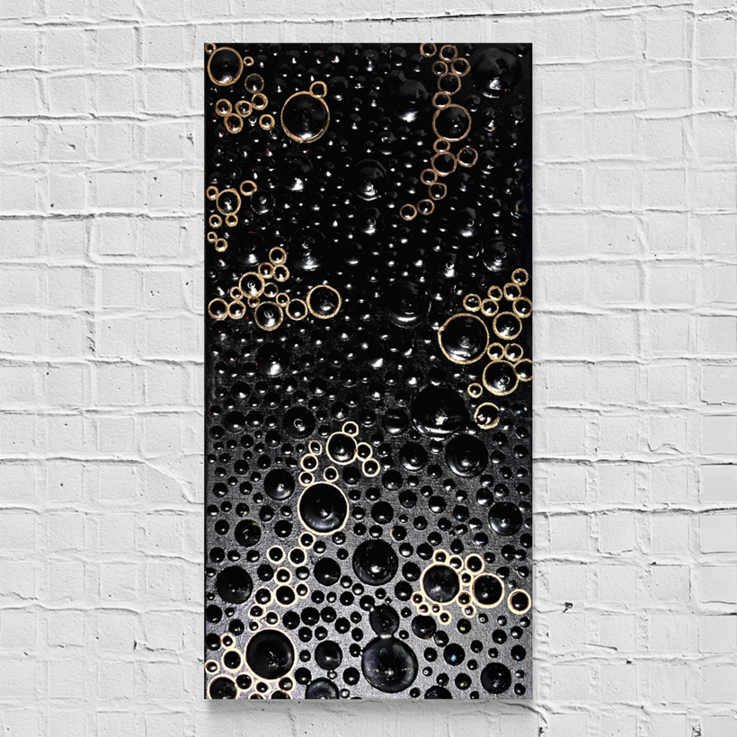 A rectangular black abstract wall art piece featuring raised metallic gold and black bubble-like circular patterns, displayed against a white painted brick wall.