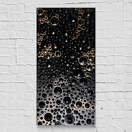 A rectangular black abstract wall art piece featuring raised metallic gold and black bubble-like circular patterns, displayed against a white painted brick wall.