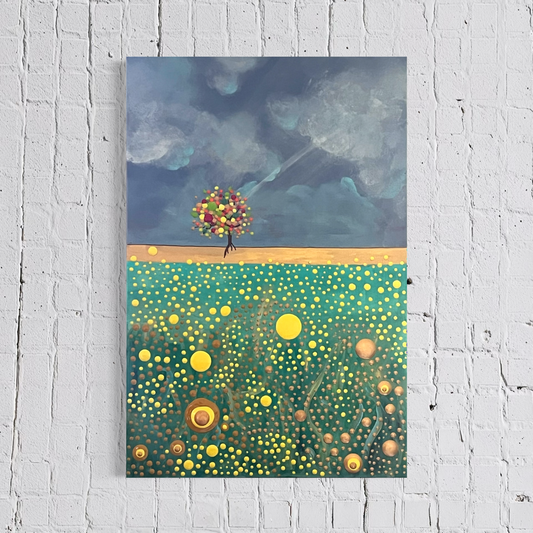 A vertical canvas painting depicting a surreal landscape with a small flower-blossomed tree on a golden path under a cloudy blue sky, above a green field dotted with yellow circles, shown hanging on a white brick wall.